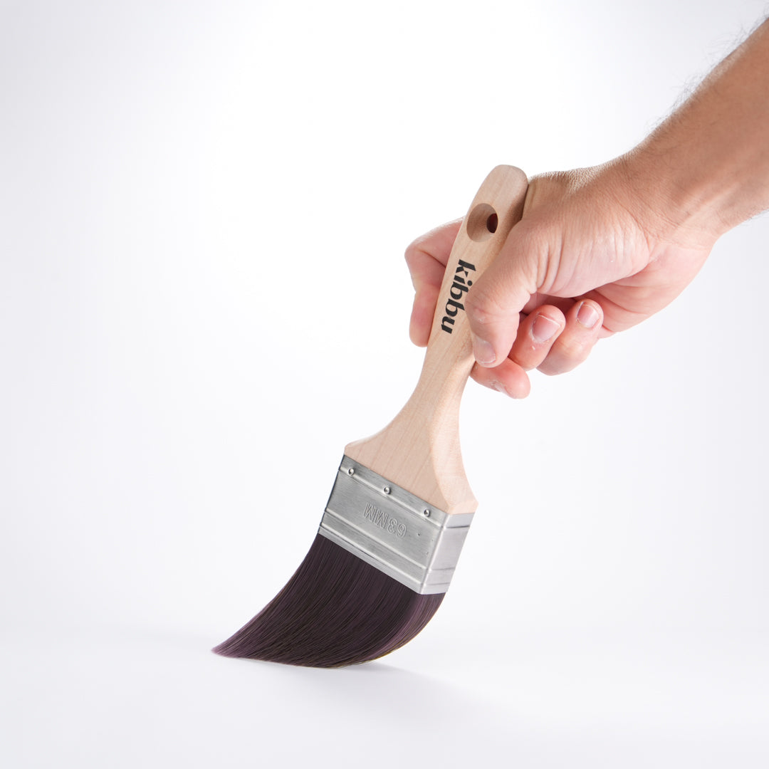 Hand holding a Kibbu paint brush with wooden handle on a white background
